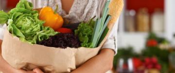Photo of a woman holding a paper bag full of fresh vegetables.