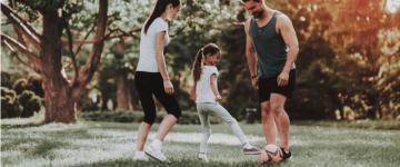 Photo of a happy young family playing soccer in a park.