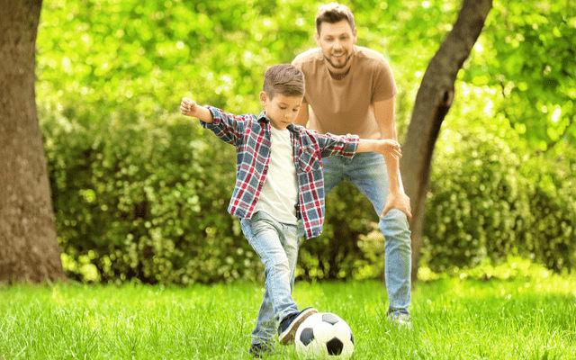 Photo of a young father playing soccer with his son at a park