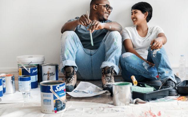 Photo of a young couple resting on the floor surrounded by painting supplies