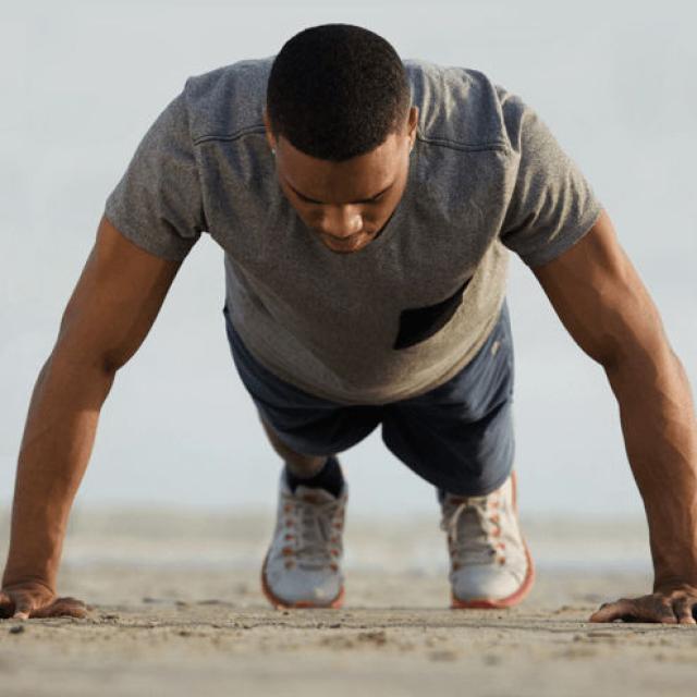 Man in the middle of doing a push-up on a beach.